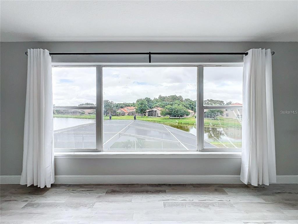 A room with light wood-look flooring and white curtains framing a large window overlooking water — 5356 WATERVISTA DRIVE, ORLANDO, FL