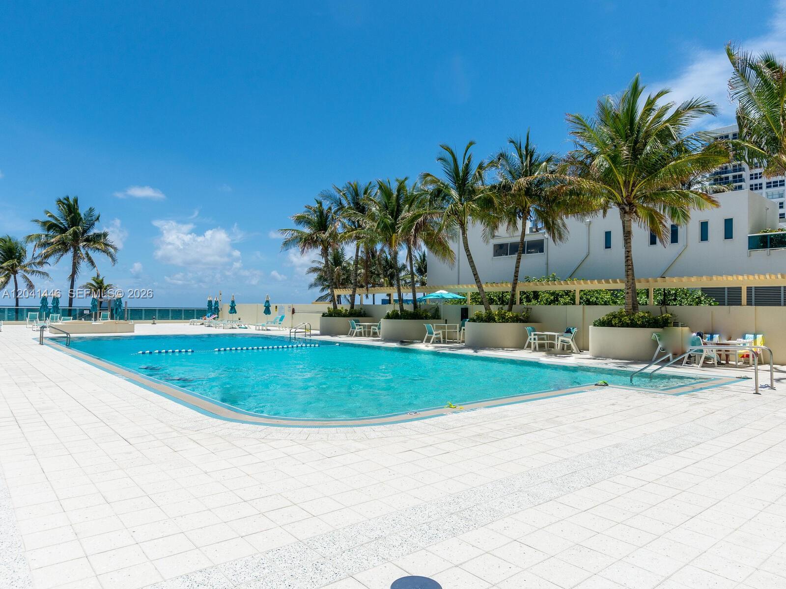 An outdoor swimming pool surrounded by a white tiled deck and palm trees — 2501 S Ocean Dr # 327, Hollywood FL 33019, HOLLYWOOD, FL