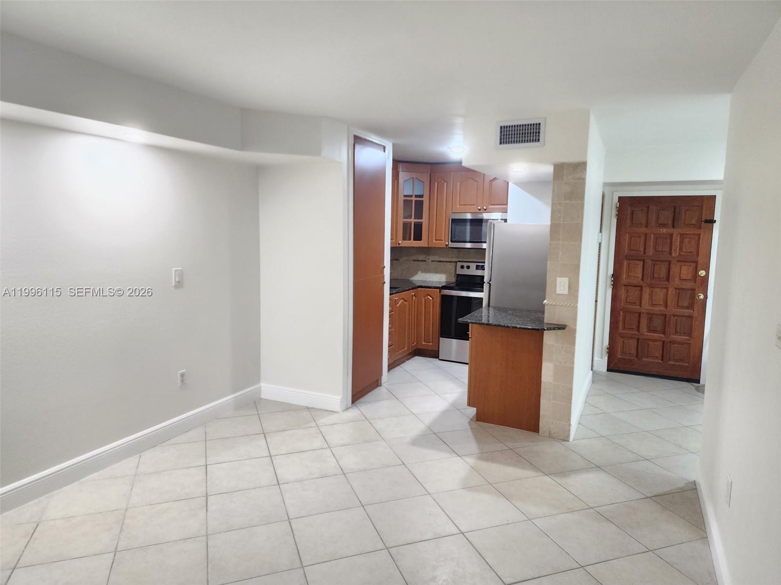 A kitchen with wood cabinets and stainless steel appliances opens to a tiled living area — 1800 NW 24th Ave # 415, Miami FL 33125, MIAMI, FL