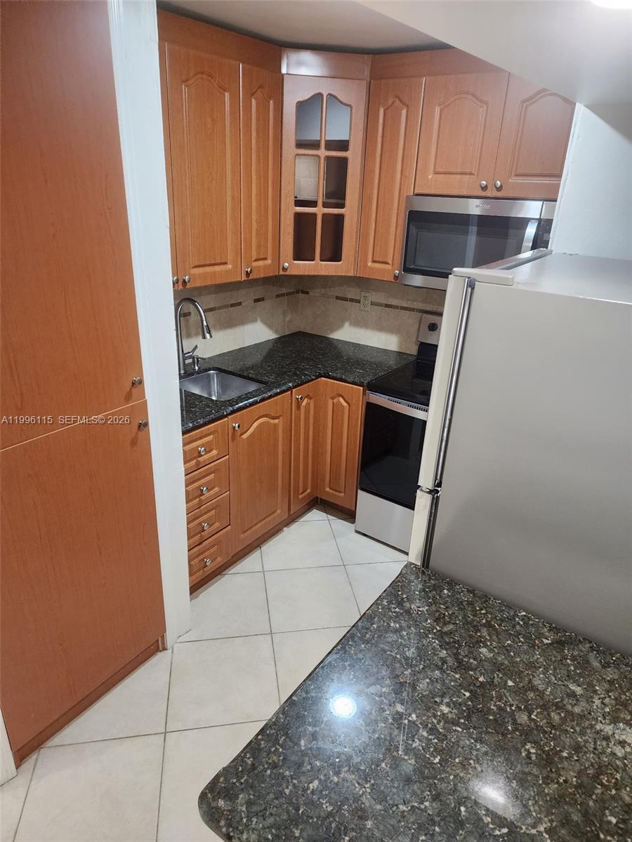 A small kitchen features wood cabinets, dark granite countertops, and stainless steel appliances — 1800 NW 24th Ave # 415, Miami FL 33125, MIAMI, FL