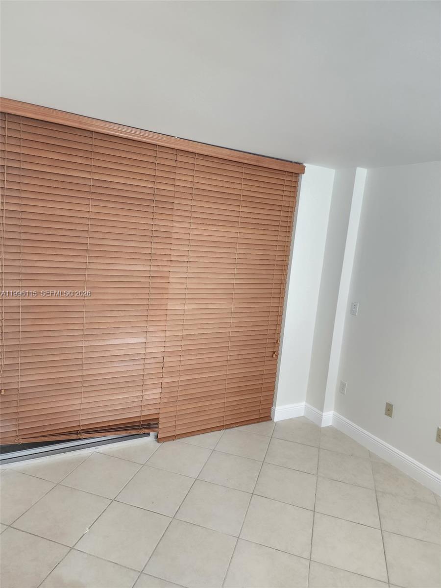 A room with light-colored tile flooring and wooden blinds covering a large sliding glass door — 1800 NW 24th Ave # 415, Miami FL 33125, MIAMI, FL