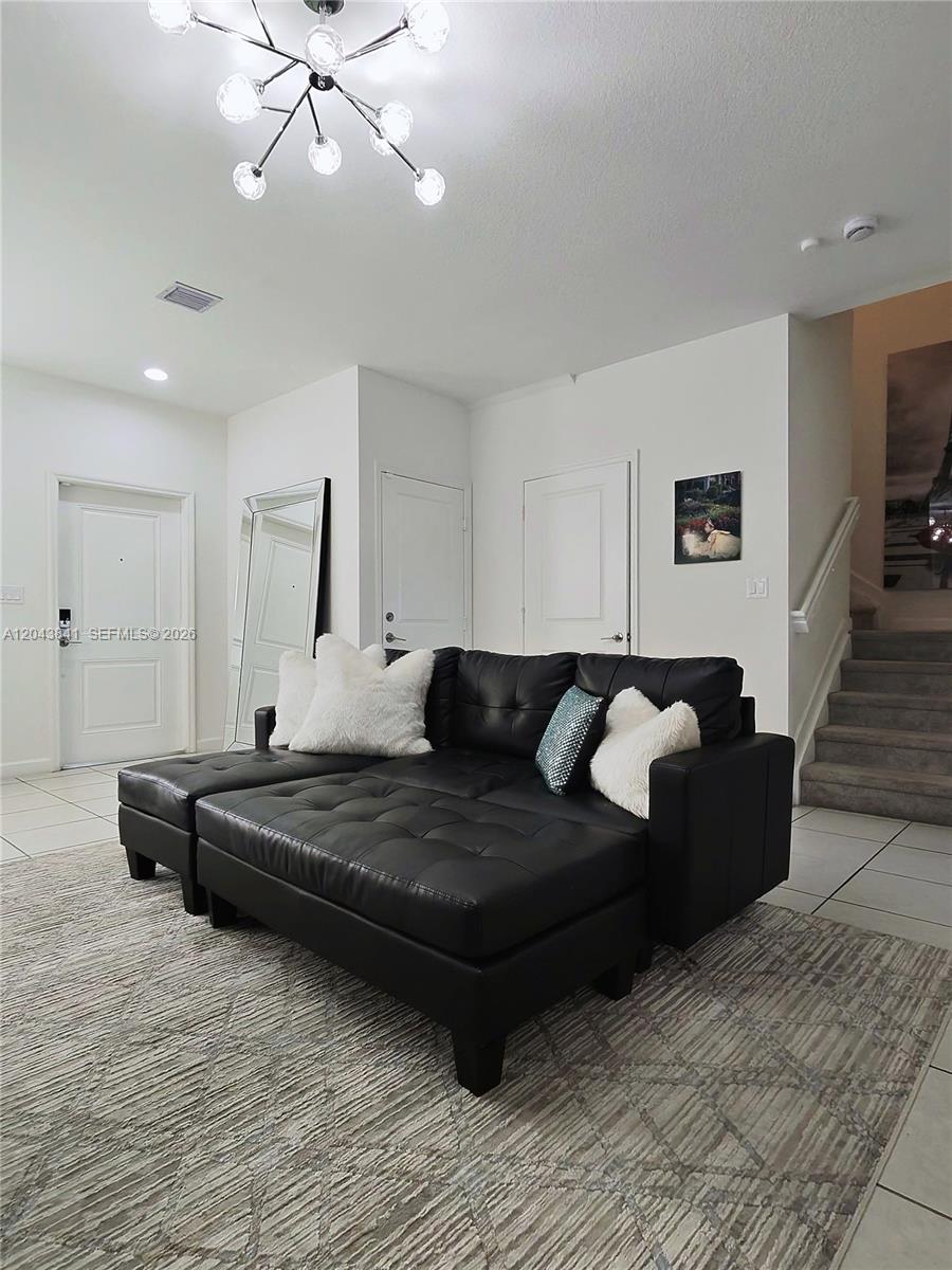 A living room features a black tufted sectional sofa, a modern chandelier, and carpeted stairs — 23013 SW 128th Pl, Miami FL 33170, MIAMI, FL