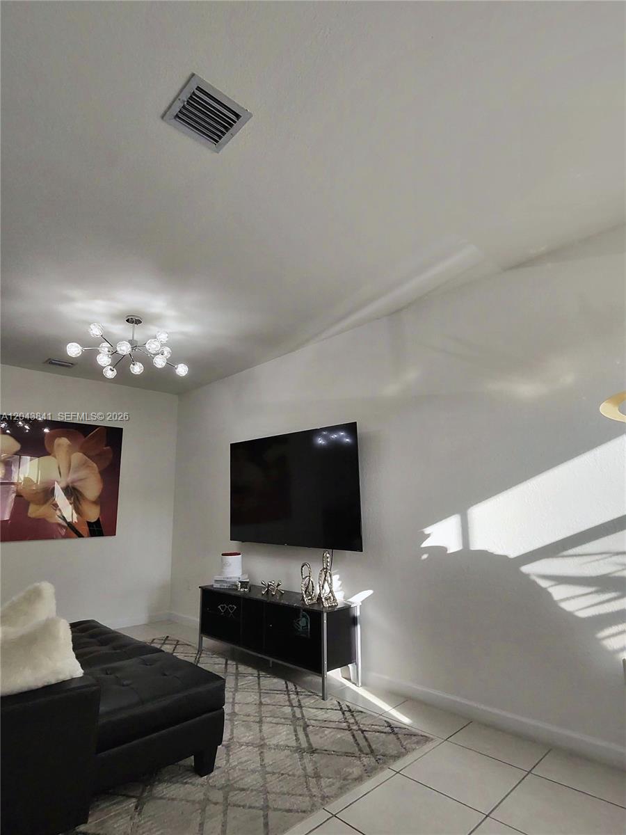 A living room features a wall-mounted television, a black media console, and a modern chandelier — 23013 SW 128th Pl, Miami FL 33170, MIAMI, FL