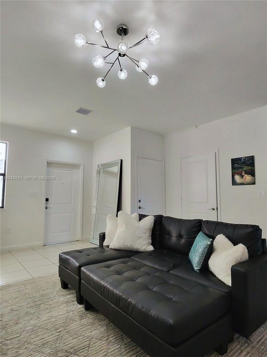 A living room features a black tufted sectional sofa, a modern chandelier, and white walls — 23013 SW 128th Pl, Miami FL 33170, MIAMI, FL