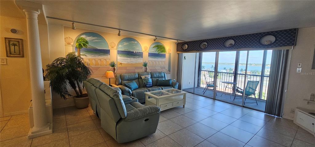 A living room features light blue leather furniture, a mural, and a balcony with water views — 10355 PARADISE BOULEVARD UNIT 710, TREASURE ISLAND, FL