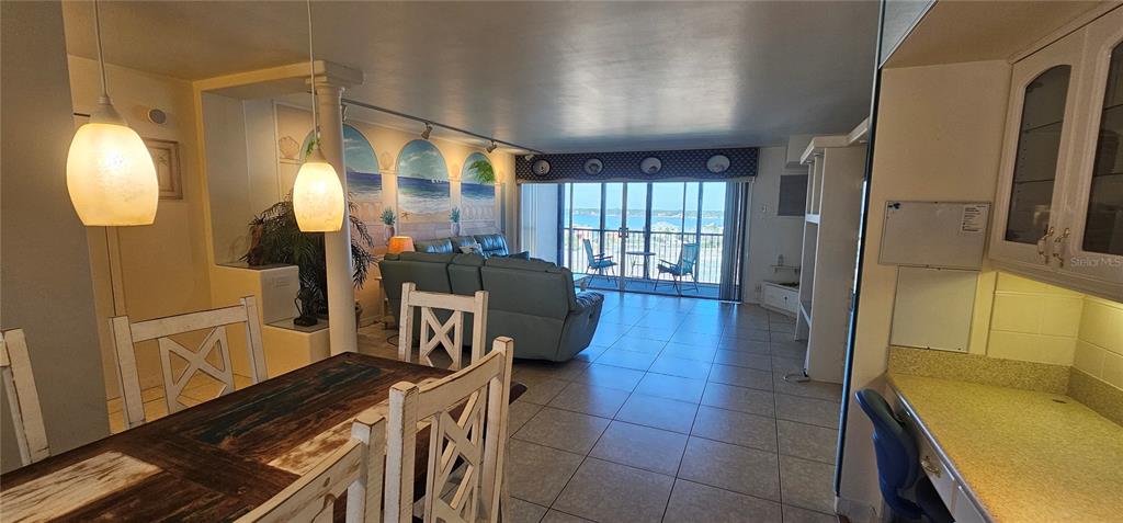 An open-concept living and dining area features tile floors, a mural, and a balcony view — 10355 PARADISE BOULEVARD UNIT 710, TREASURE ISLAND, FL