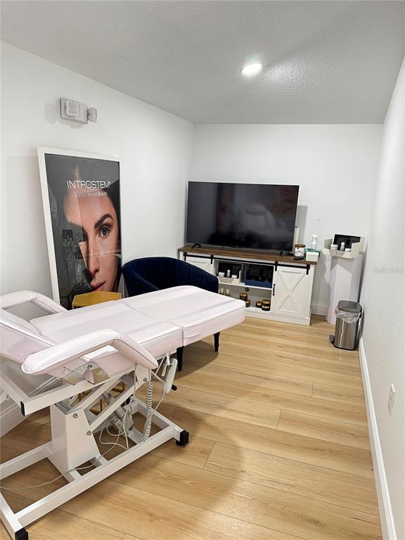 A treatment room features a pink medical bed, a television on a console, and wood-look flooring — 411 FLAGLER AVENUE, NEW SMYRNA BEACH, FL