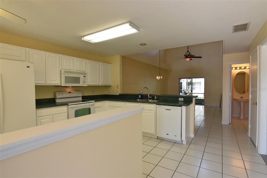 A kitchen with white cabinets, green countertops, and tile flooring opens to a living area — 2203 CYPRESS KNEE LOOP, KISSIMMEE, FL