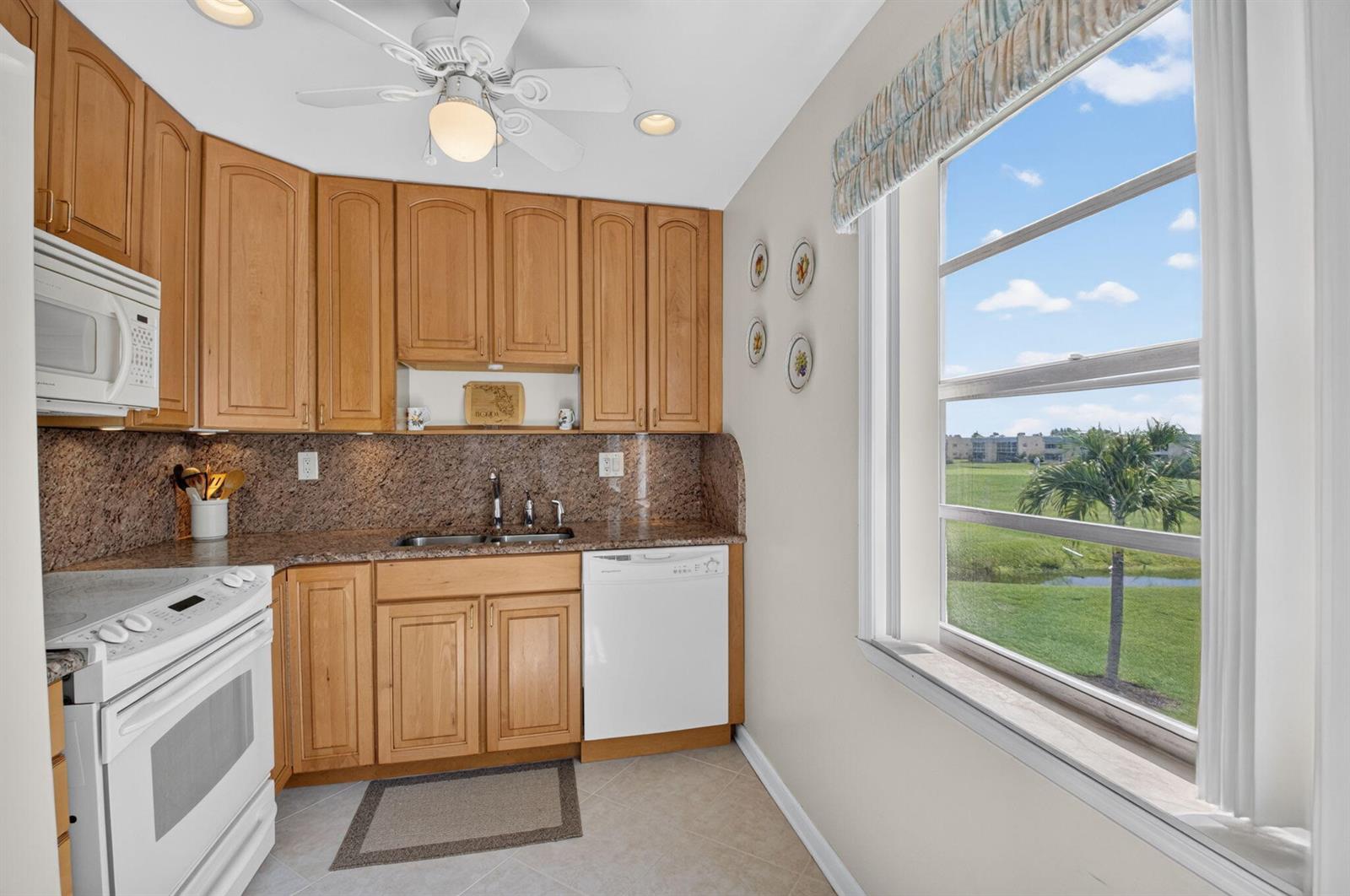 A kitchen with light wood cabinets, granite countertops, white appliances, and a view of greenery — 323 Capri G # 323, Delray Beach FL 33484, DELRAY BEACH, FL