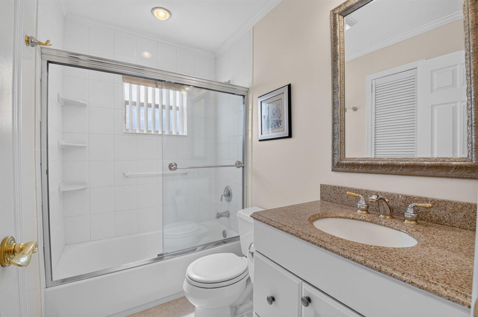 A bathroom features a white vanity with a granite countertop, toilet, and a glass-enclosed shower — 323 Capri G # 323, Delray Beach FL 33484, DELRAY BEACH, FL
