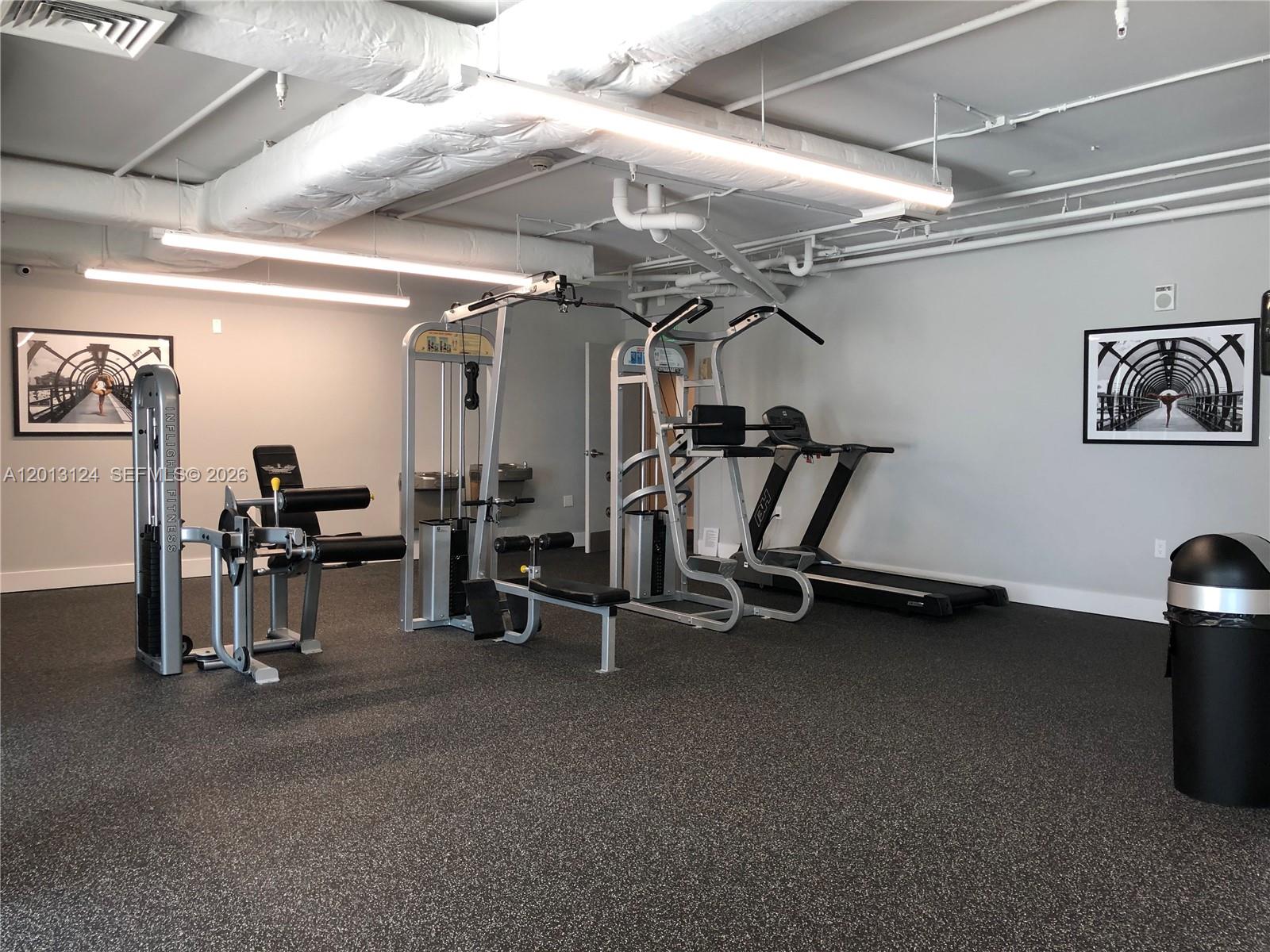A gym room features exercise equipment, rubber flooring, and exposed ceiling pipes — 140 S Dixie Hwy # 1025, Hollywood FL 33020, HOLLYWOOD, FL