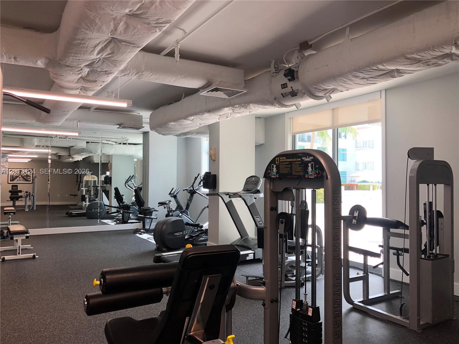 A gym features various exercise machines, mirrored walls, and exposed ductwork on the ceiling — 140 S Dixie Hwy # 1025, Hollywood FL 33020, HOLLYWOOD, FL