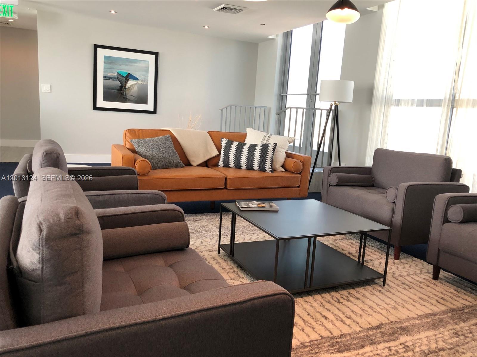 A living room features a brown leather sofa, gray armchairs, a coffee table, and artwork — 140 S Dixie Hwy # 1025, Hollywood FL 33020, HOLLYWOOD, FL