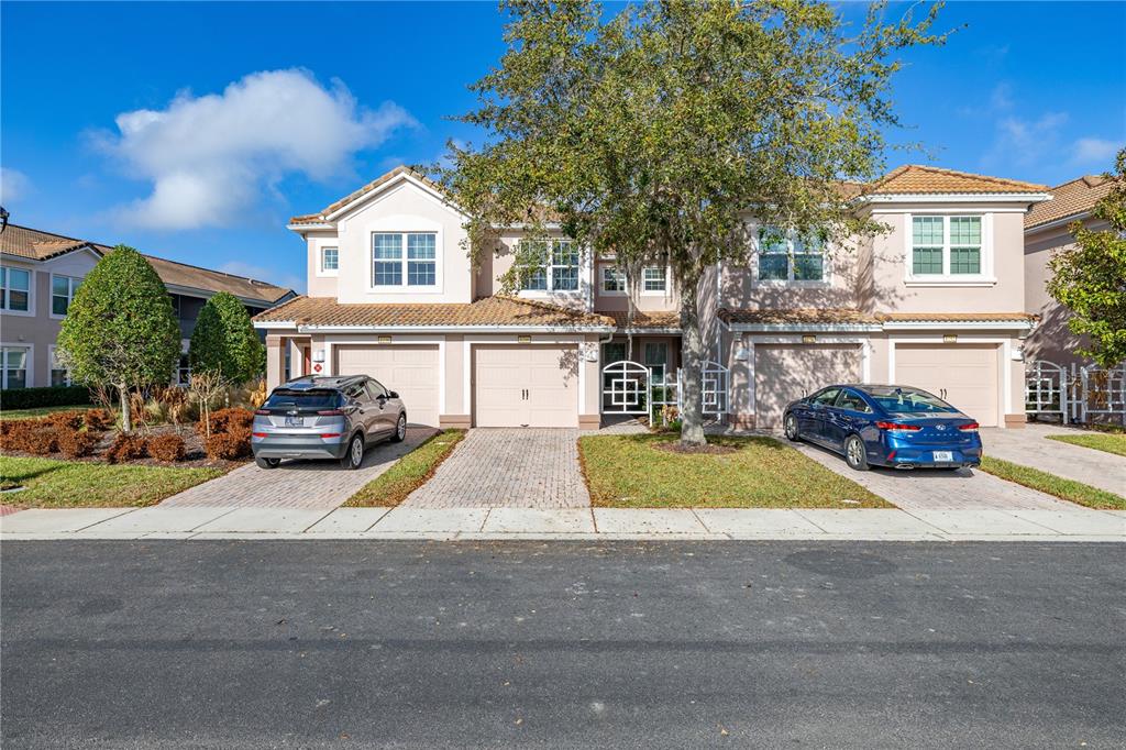 A two-story townhouse exterior with a paved driveway, two garages, and a large front tree — 1256 ROMANI AVENUE, DAVENPORT, FL