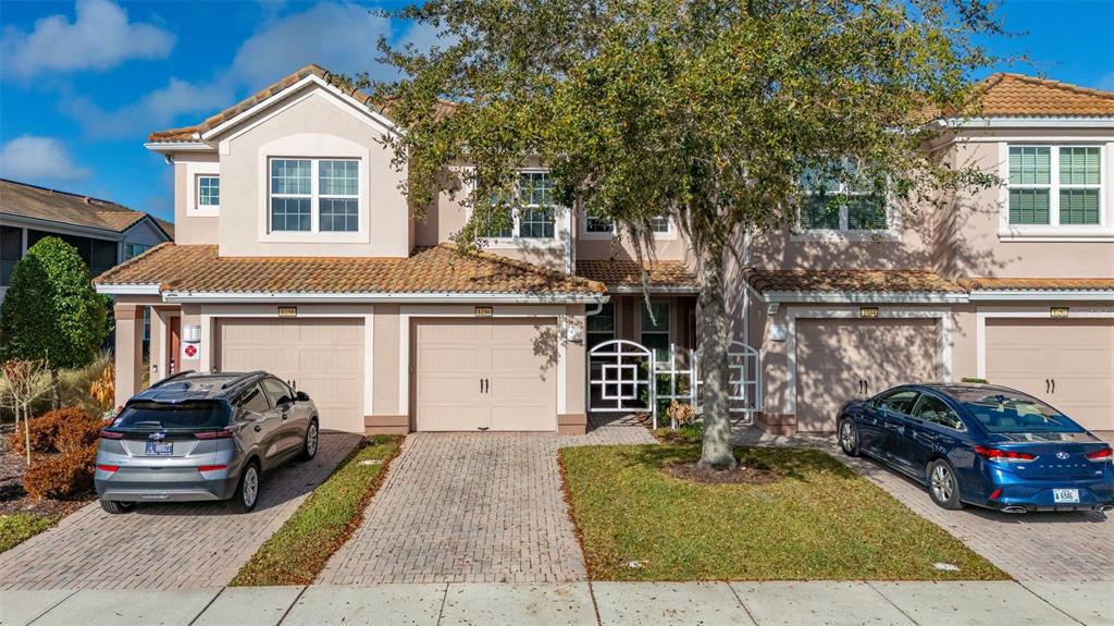 A two-story townhouse exterior with a beige facade, tile roof, and two parked cars — 1256 ROMANI AVENUE, DAVENPORT, FL