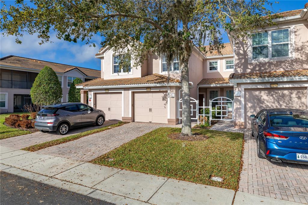 A two-story townhouse exterior with two garage doors, a paved driveway, and parked cars — 1256 ROMANI AVENUE, DAVENPORT, FL