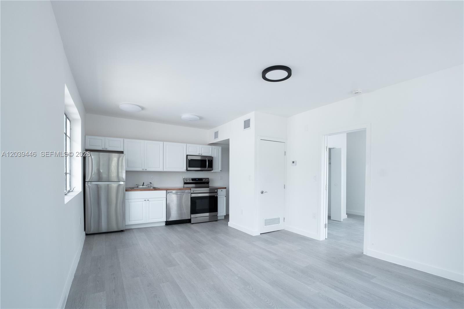 A kitchen with white cabinets and stainless steel appliances sits in a minimalist room — 423 NE 71st St # 4, Miami FL 33138, MIAMI, FL
