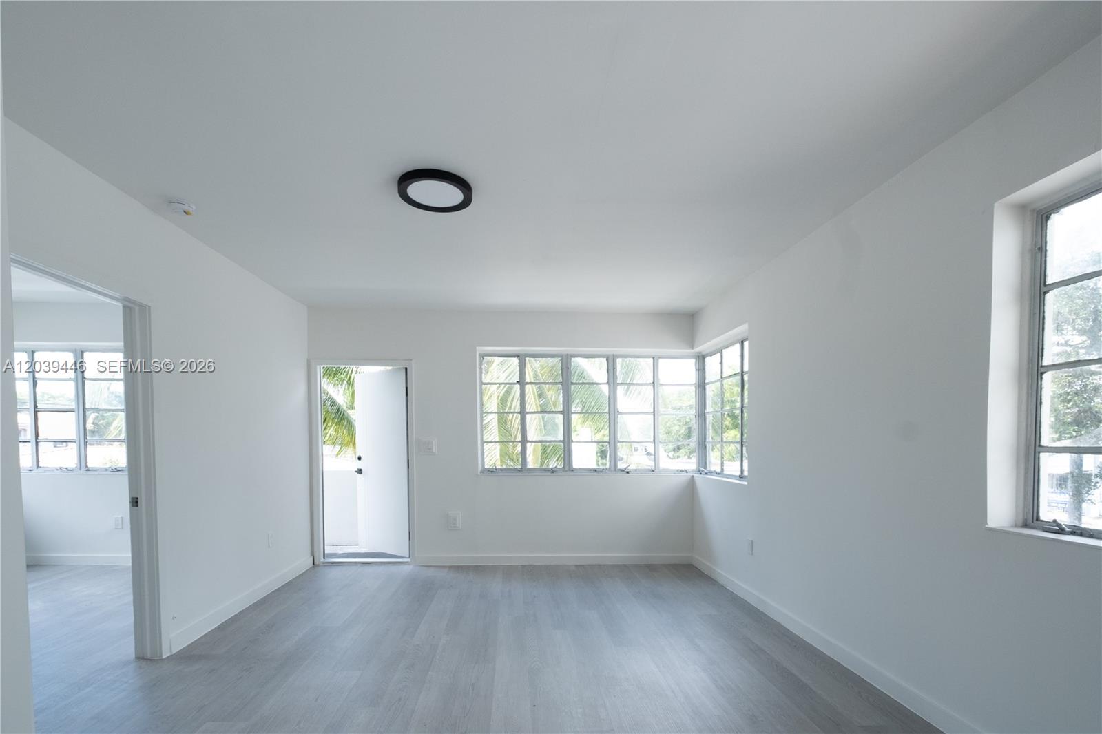 An empty room features white walls, light wood-look flooring, and multiple windows with exterior views — 423 NE 71st St # 4, Miami FL 33138, MIAMI, FL