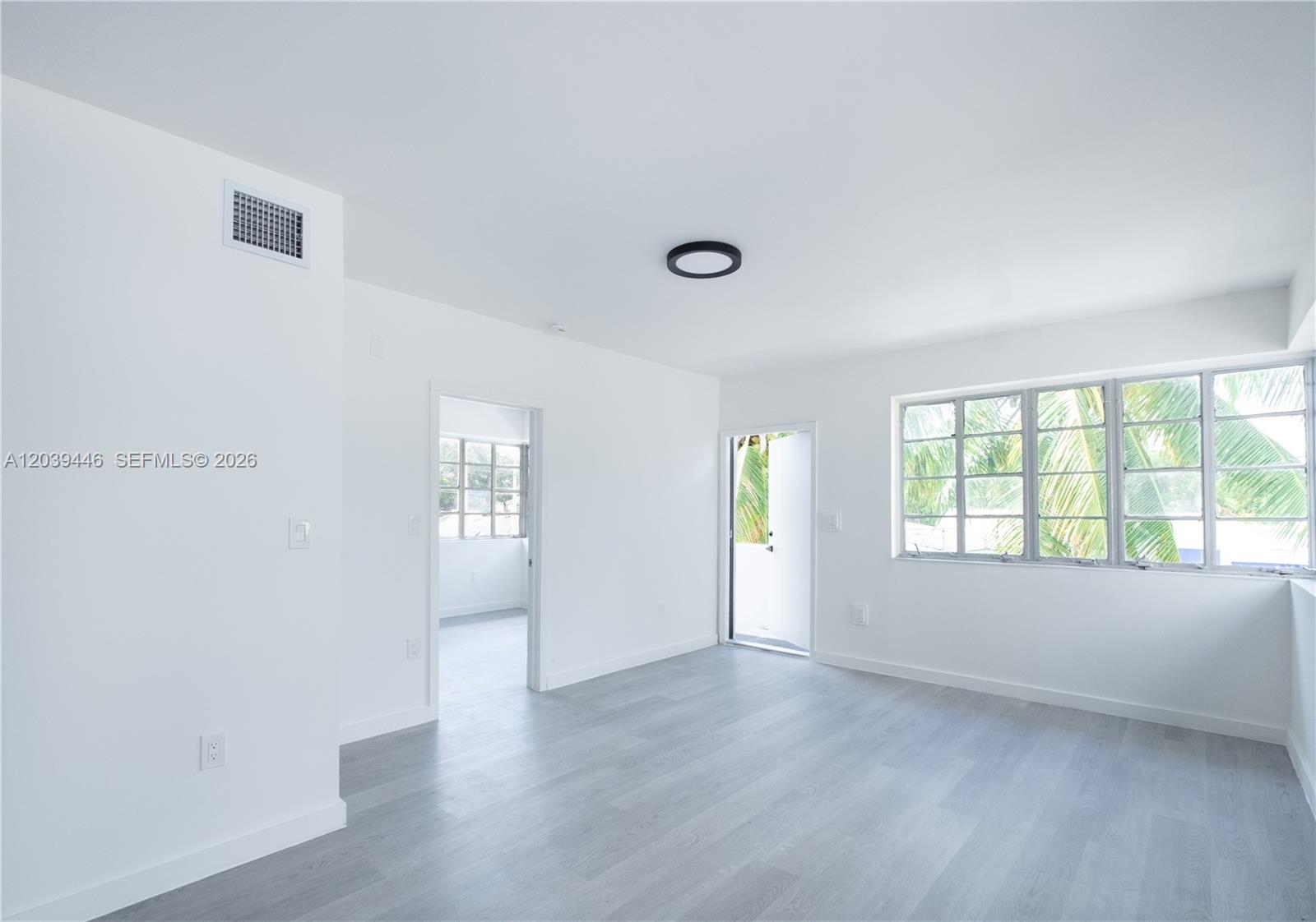 A bright, empty room features white walls, light gray wood-look flooring, and large windows — 423 NE 71st St # 4, Miami FL 33138, MIAMI, FL