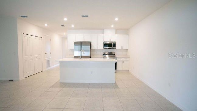 A kitchen features white cabinetry, stainless steel appliances, and a central island on tiled flooring — TBD SW 80TH WAY, GAINESVILLE, FL