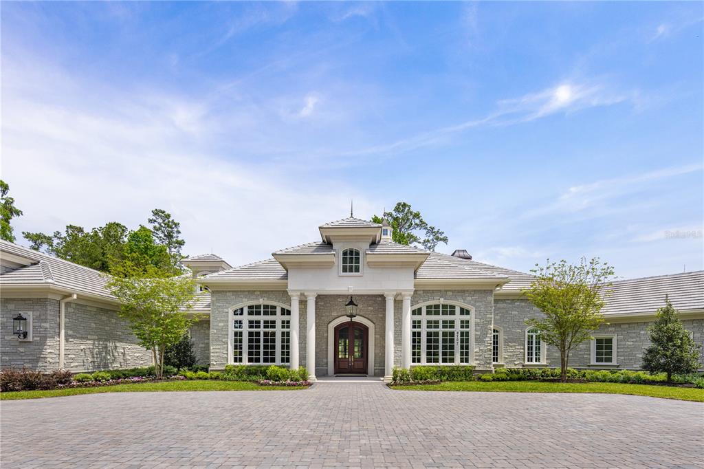 A stone-clad single-story house features a columned entryway, arched windows, and a paved driveway — 8707 NW 31ST LANE ROAD, OCALA, FL