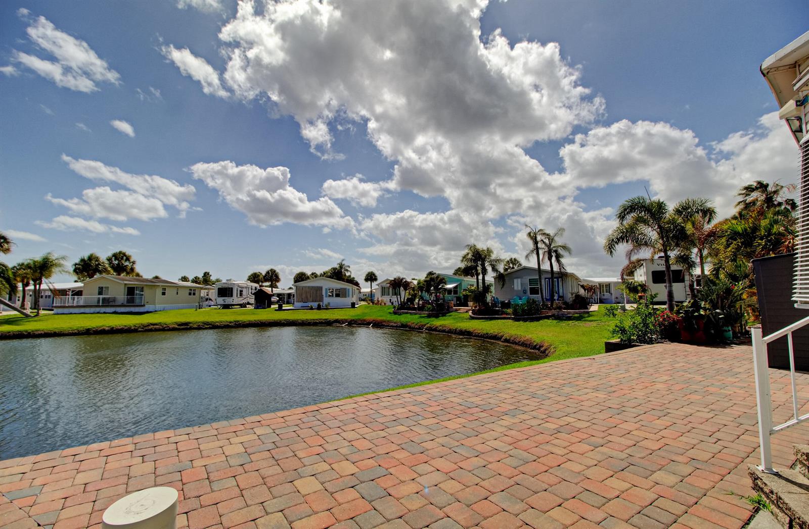 A brick patio overlooks a small pond surrounded by mobile homes and palm trees — 6430 SE 51st Street, Okeechobee FL 34974, OKEECHOBEE, FL