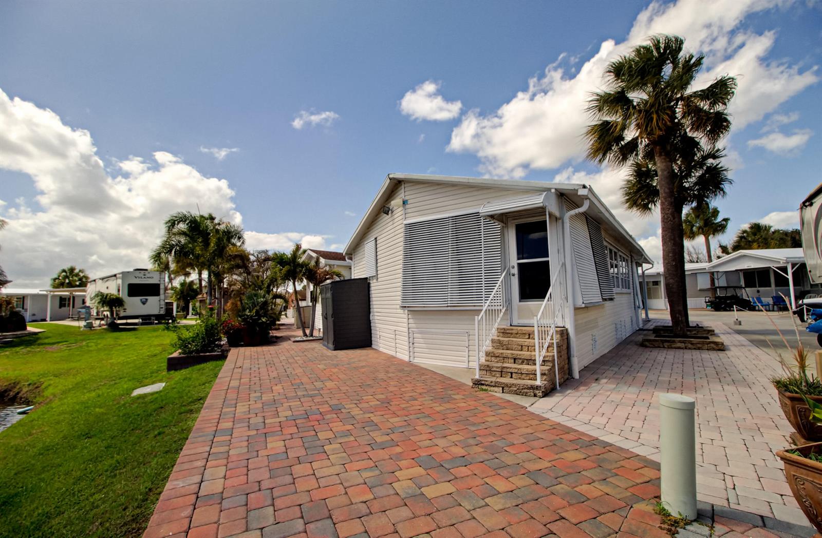 A light-colored mobile home features a brick paver patio and a palm tree outside — 6430 SE 51st Street, Okeechobee FL 34974, OKEECHOBEE, FL