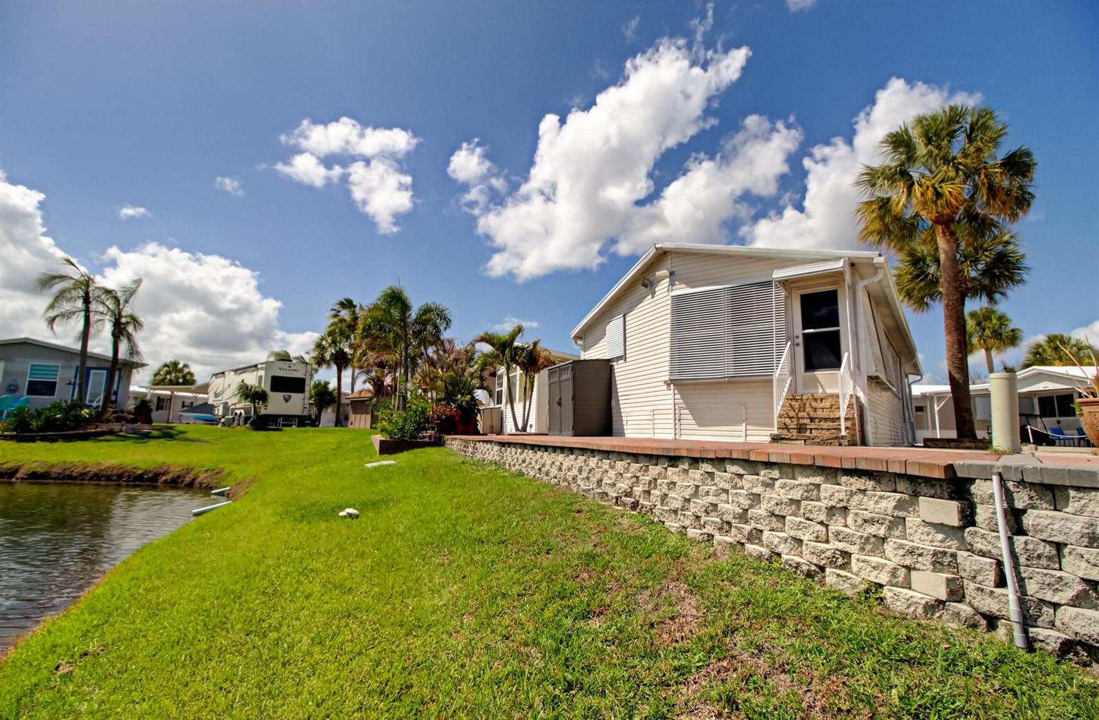 A manufactured home sits on a grassy lot beside a pond with a retaining wall — 6430 SE 51st Street, Okeechobee FL 34974, OKEECHOBEE, FL
