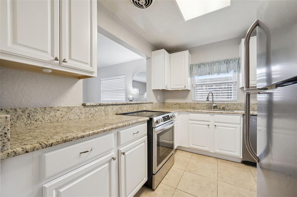 A kitchen features white cabinets, granite countertops, and a stainless steel stove below a pass-through window — 2513 MUSSELWHITE AVENUE, ORLANDO, FL