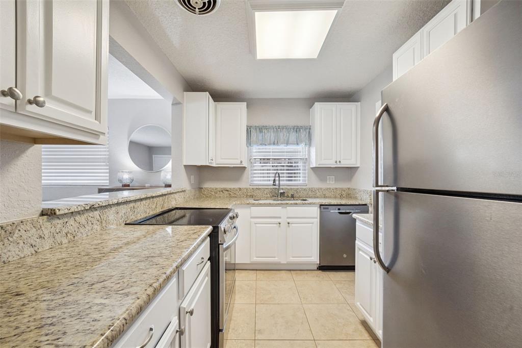 A kitchen features white cabinets, granite countertops, stainless steel appliances, and tile flooring — 2513 MUSSELWHITE AVENUE, ORLANDO, FL