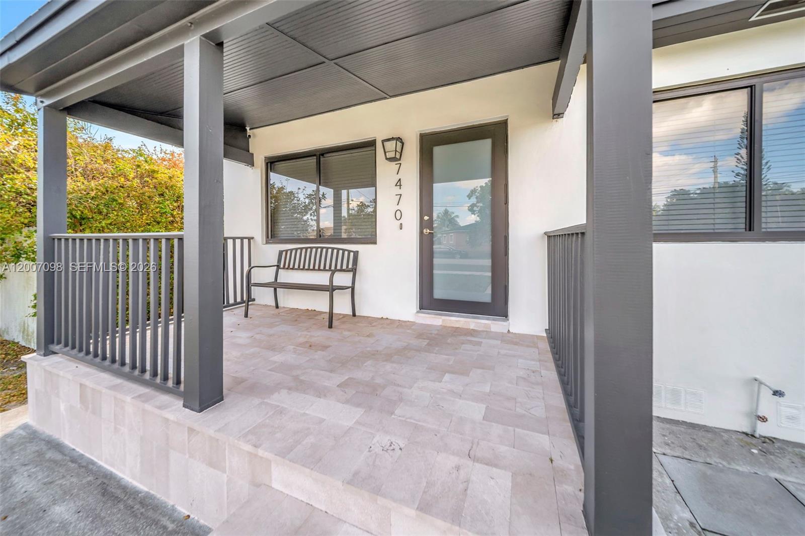 A covered porch features tiled flooring, a metal bench, and a glass-paneled front door — 7470 SW 37th St, Miami FL 33155, MIAMI, FL
