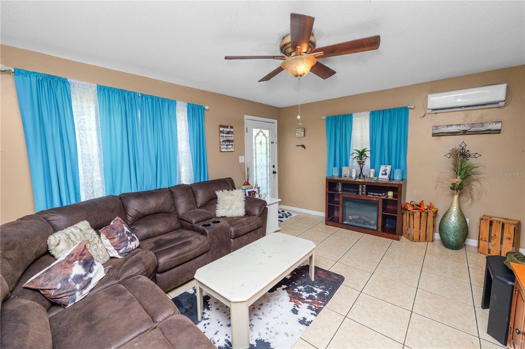 A living room features a brown sectional sofa, tile flooring, a ceiling fan, and curtains — 517 TANGLEWOOD DRIVE, AUBURNDALE, FL