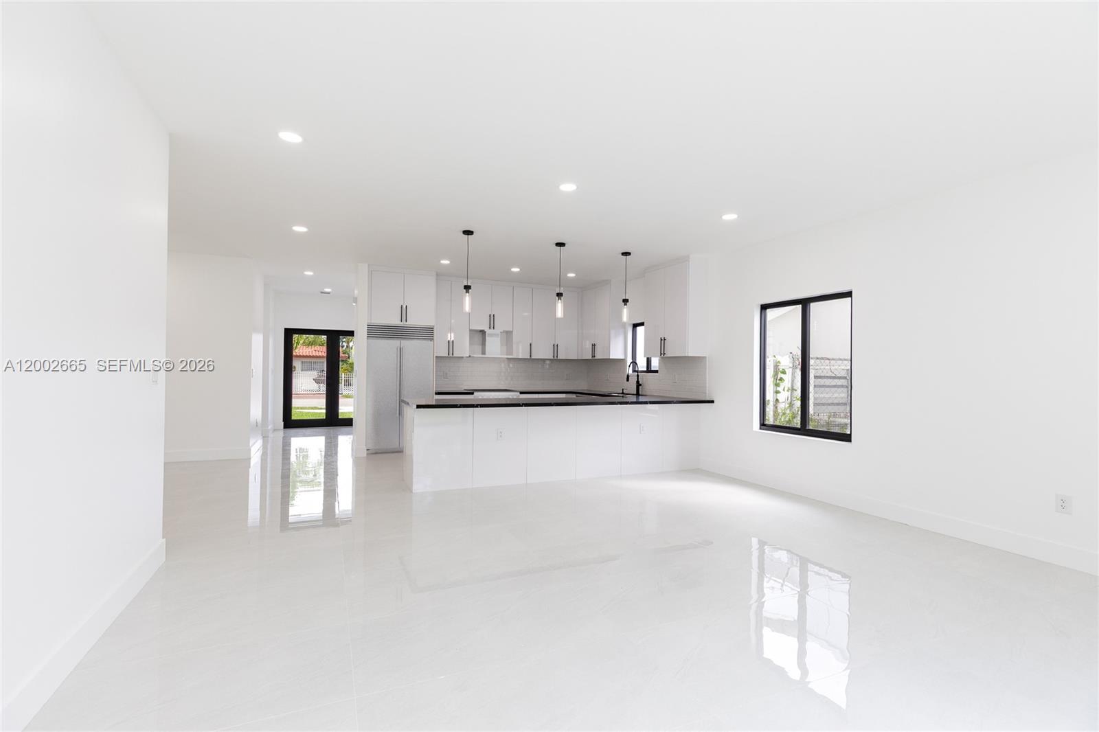 A modern kitchen with white cabinets and a black countertop opens to a living area — 5550 SW 4th St, Miami FL 33134, MIAMI, FL