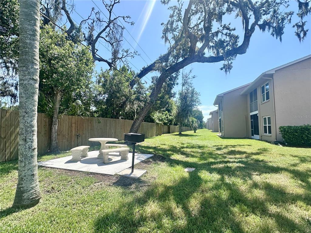 A concrete patio with a picnic table and grill sits beside an apartment building — 6440 SPRING FLOWER DRIVE UNIT 12, NEW PORT RICHEY, FL