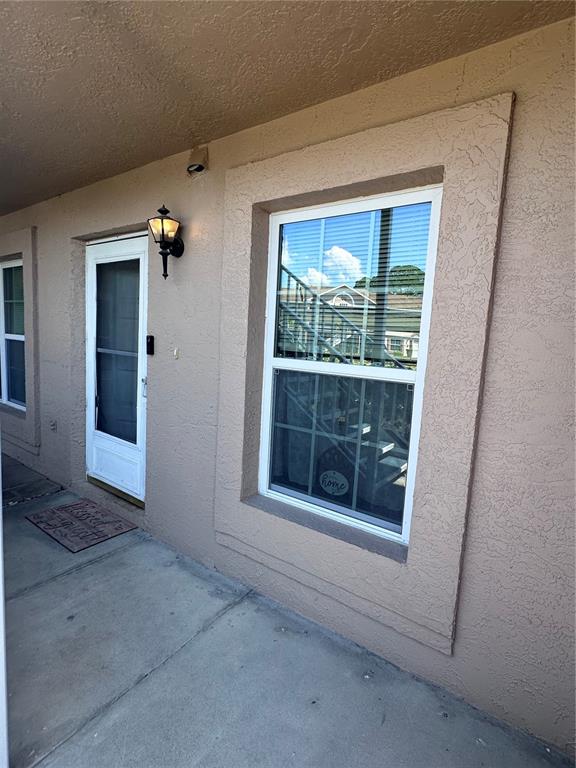 A beige exterior wall features a white door, a window with blinds, and a wall lamp — 6440 SPRING FLOWER DRIVE UNIT 12, NEW PORT RICHEY, FL