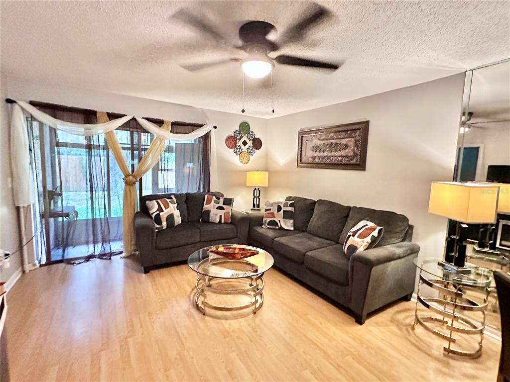 A living room features dark gray sofas, a glass coffee table, and light wood flooring — 6440 SPRING FLOWER DRIVE UNIT 12, NEW PORT RICHEY, FL