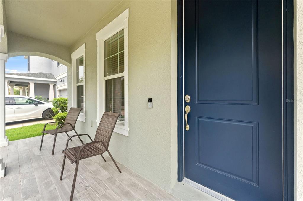 A covered front porch features a dark blue door, two chairs, and light-colored tile flooring — 14722 ROCKY BROOK DRIVE, TAMPA, FL