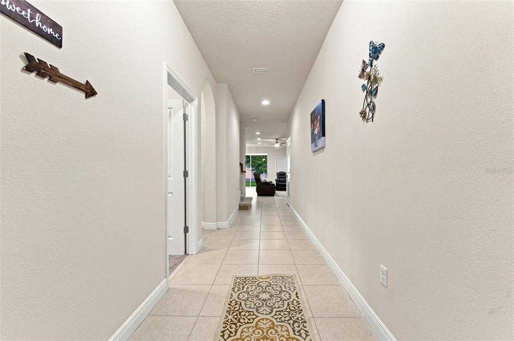 A long, tiled hallway leads toward a living area with a view of the backyard — 14722 ROCKY BROOK DRIVE, TAMPA, FL