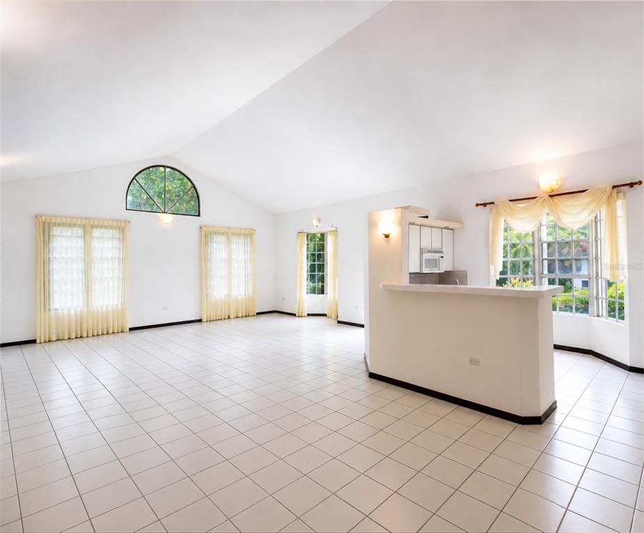 A spacious living area with white tile floors, vaulted ceilings, and an open kitchen counter — 160 CAMINO DE LAS POMARROSAS URB. HACIENDA SABANERA, CIDRA, PR