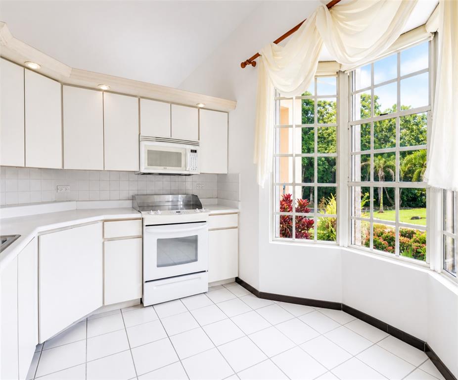 A white kitchen features tile flooring, white cabinetry, and a large bay window with curtains — 160 CAMINO DE LAS POMARROSAS URB. HACIENDA SABANERA, CIDRA, PR