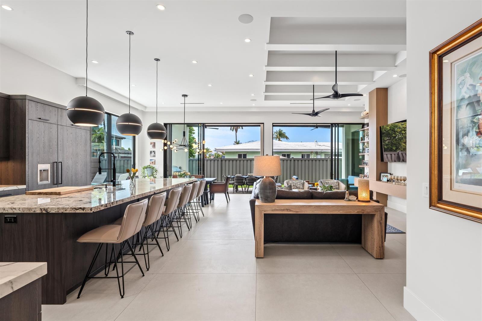 A modern open-concept kitchen and living area features a large island, pendant lights, and sliding doors — 2880 NE 35th Street, Lighthouse Point FL 33064, LIGHTHOUSE POINT, FL