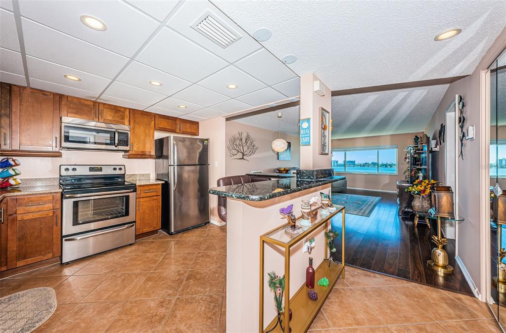 A kitchen with wood cabinets and stainless steel appliances opens to a living area — 4750 COVE CIRCLE UNIT 605, ST PETERSBURG, FL