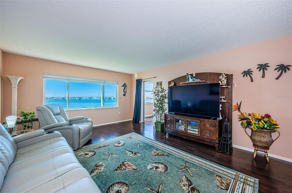 A living room features a large window with a water view, light-colored furniture, and flooring — 4750 COVE CIRCLE UNIT 605, ST PETERSBURG, FL
