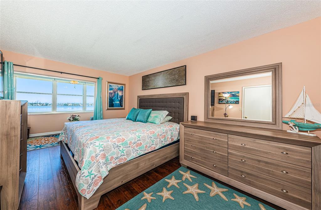 A bedroom with a queen bed, wooden dresser, and a large window overlooking the water — 4750 COVE CIRCLE UNIT 605, ST PETERSBURG, FL