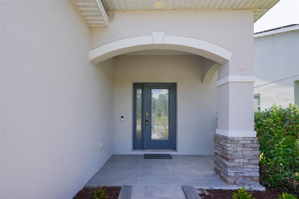A covered front porch features a gray front door with glass panels and stone accents — 173 VILLAVISTA COURT, DAVENPORT, FL