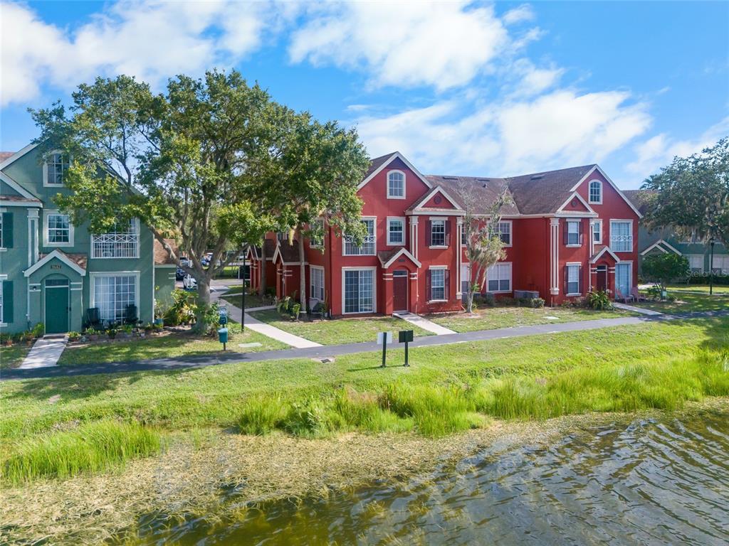 A red multi-story apartment building sits beside a grassy lawn and a pond — 9638 LAKE CHASE ISLAND WAY UNIT 9638, TAMPA, FL