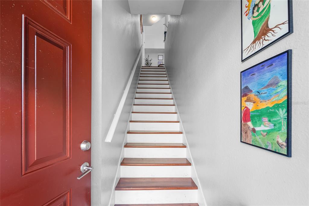 A staircase with wooden treads and white risers leads upward beside a red door — 9638 LAKE CHASE ISLAND WAY UNIT 9638, TAMPA, FL