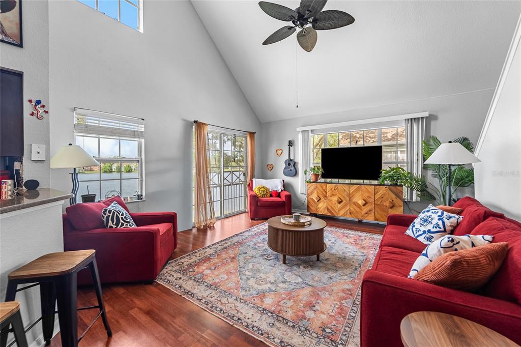 A living room with a vaulted ceiling, red furniture, a patterned rug, and lake views — 9638 LAKE CHASE ISLAND WAY UNIT 9638, TAMPA, FL