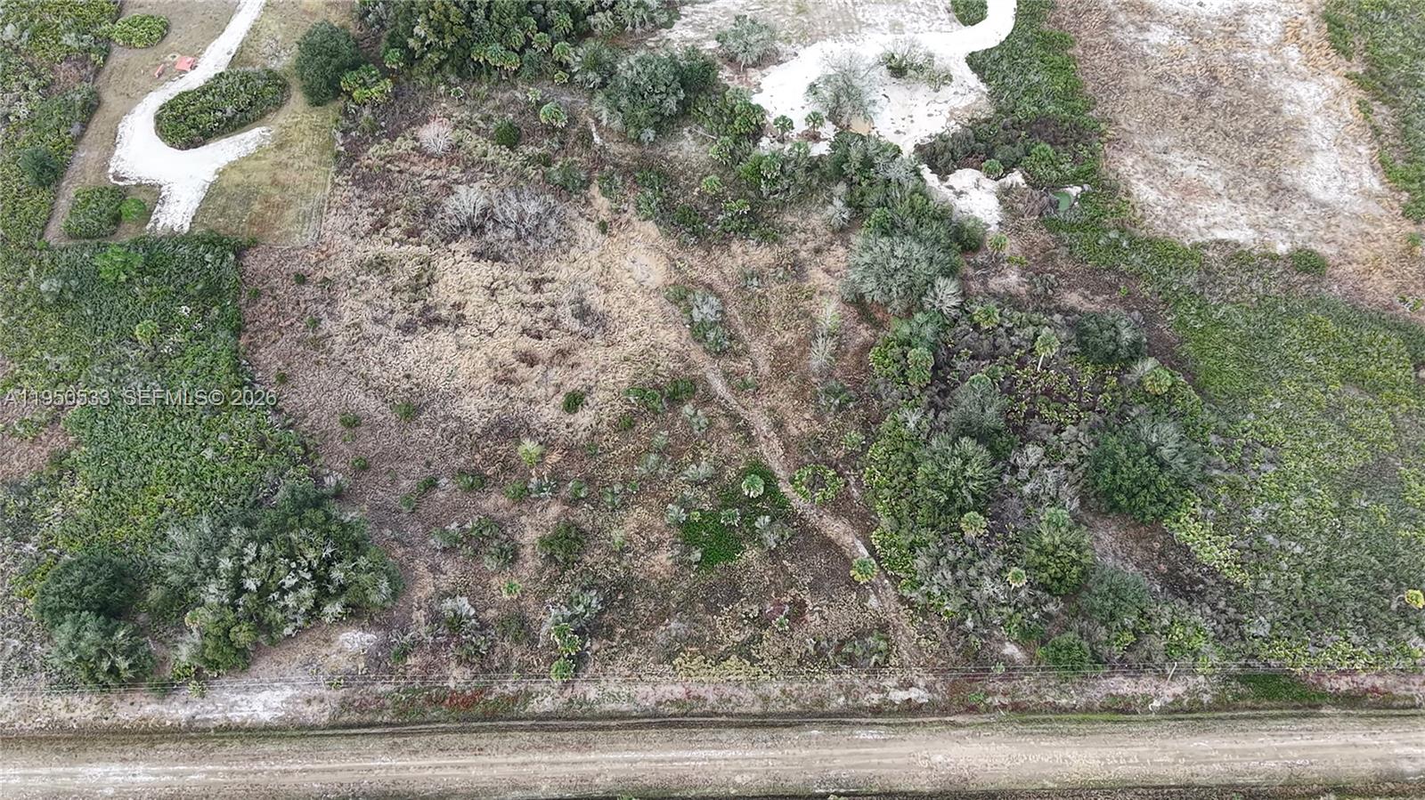 An aerial view shows a rural, undeveloped plot of land with vegetation and dirt paths — 21867 NW 276TH, Okeechobee FL 34972, OKEECHOBEE, FL