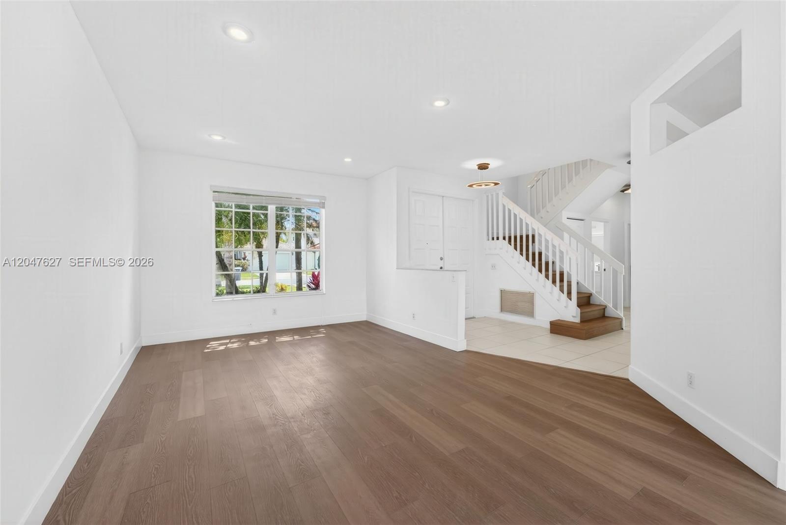 A living room features wood-look flooring, a large window, and a staircase with white railings — 9535 Fox Trot Ln, Boca Raton FL 33496, BOCA RATON, FL